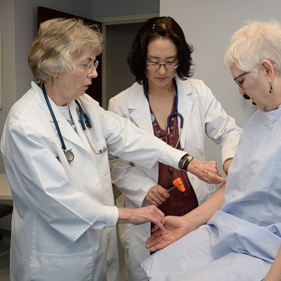 A DNP nurse being instructed on proper technique for checking reflexes with an older patient.